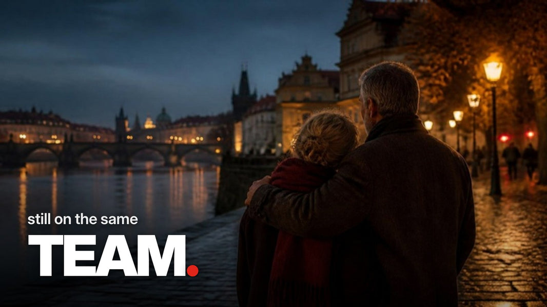 Tekst ‚still on the same TEAM.‘ boven een foto van een oudere man en vrouw die van achteren gezien innig omarmd aan een rivierpromenade in een oude stad staan tijdens de blauwe uurtjes.