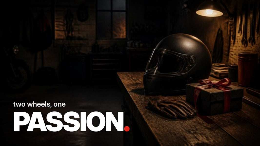 Text 'two wheels, one PASSION.' above a dark photo of a garage with a black motorcycle helmet, leather gloves, and a black-wrapped gift with a red ribbon on a workbench.