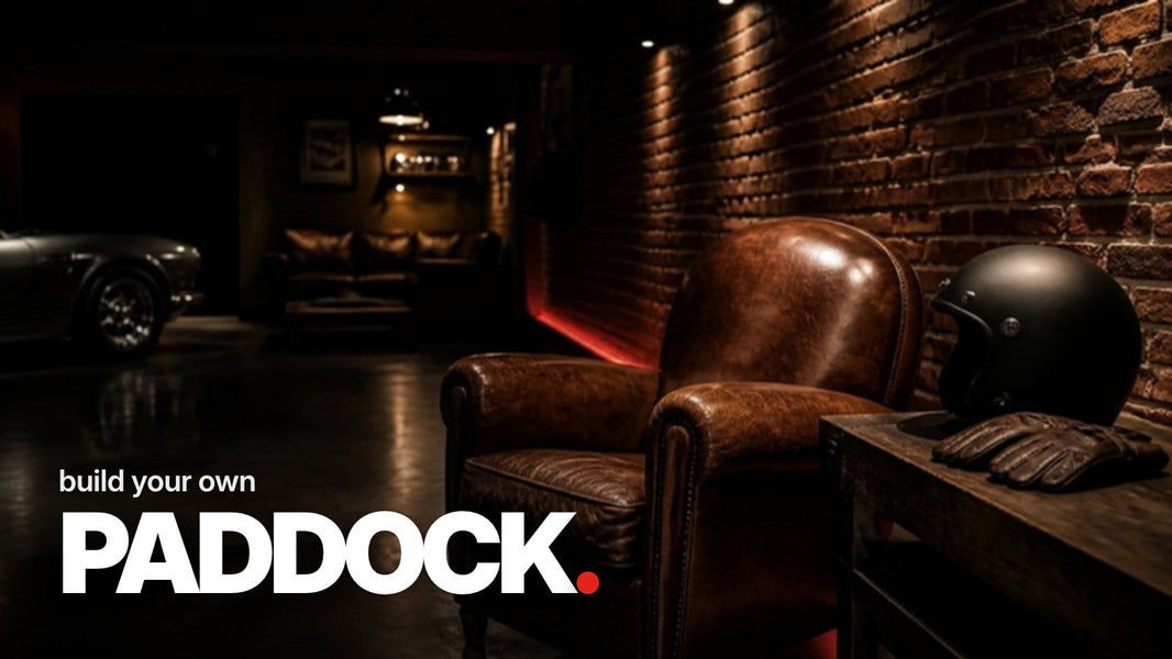 Text 'build your own PADDOCK.' above a photo of a dark basement room with a leather armchair, workbench, black helmet without logos, and red accent lighting on a brick wall.