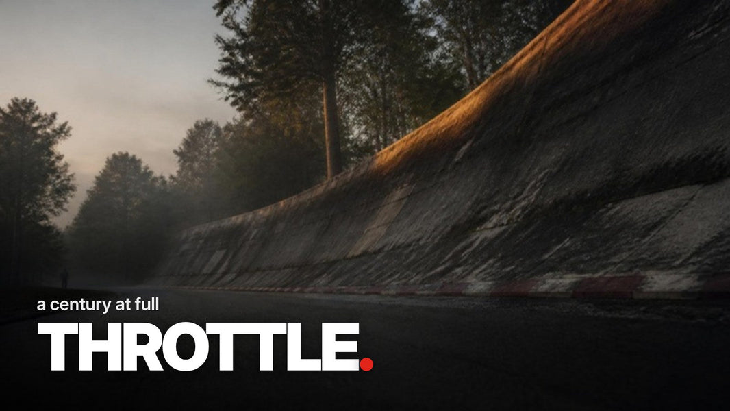 Text 'a century at full THROTTLE.' over a photo of a weathered, moss-covered concrete banked curve with red-and-white curb in a misty park at dusk.