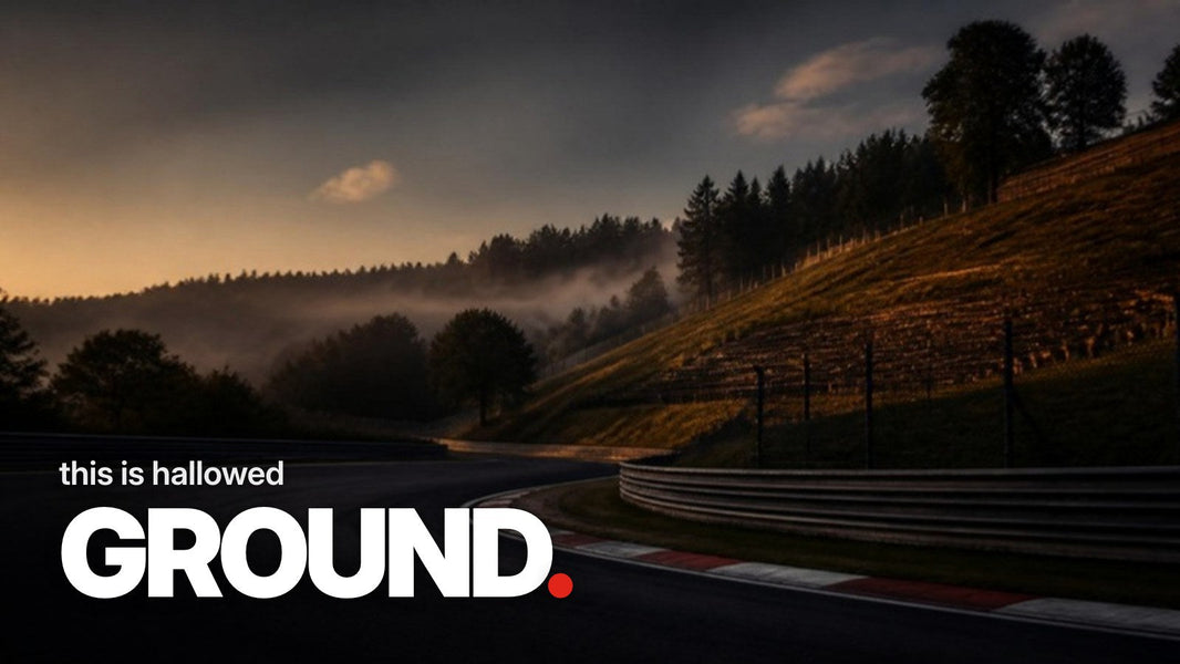 Text 'this is hallowed GROUND.' over a photo of an empty, downhill left curve with red-and-white curbs in front of a misty spectator hill at dusk.