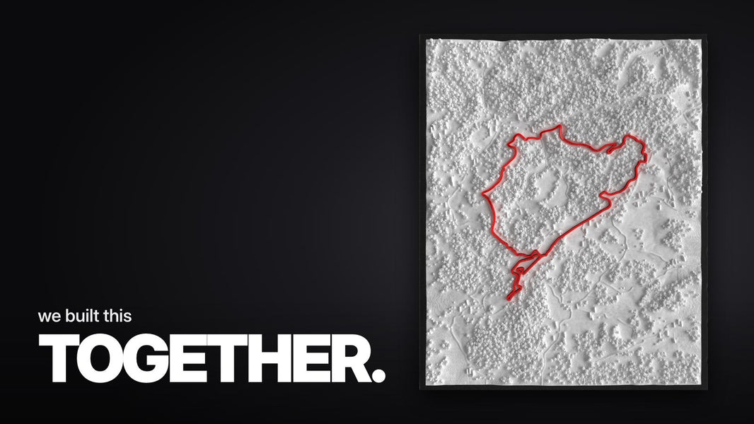 Schriftzug ‚we built this TOGETHER.‘ über dem großen Nürburgring-Rahmen mit weißem 3D-Landschaftsrelief und roter Streckenführung im schmalen schwarzen Rahmen, in Draufsicht.