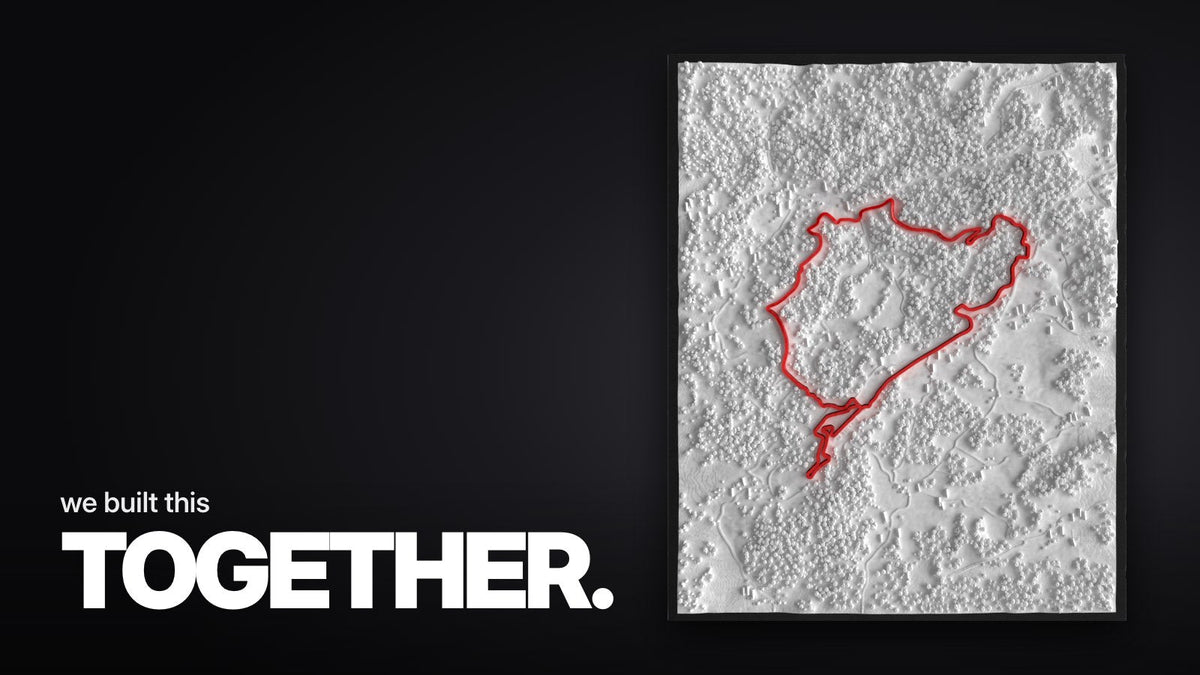 Schriftzug ‚we built this TOGETHER.‘ über dem großen Nürburgring-Rahmen mit weißem 3D-Landschaftsrelief und roter Streckenführung im schmalen schwarzen Rahmen, in Draufsicht.