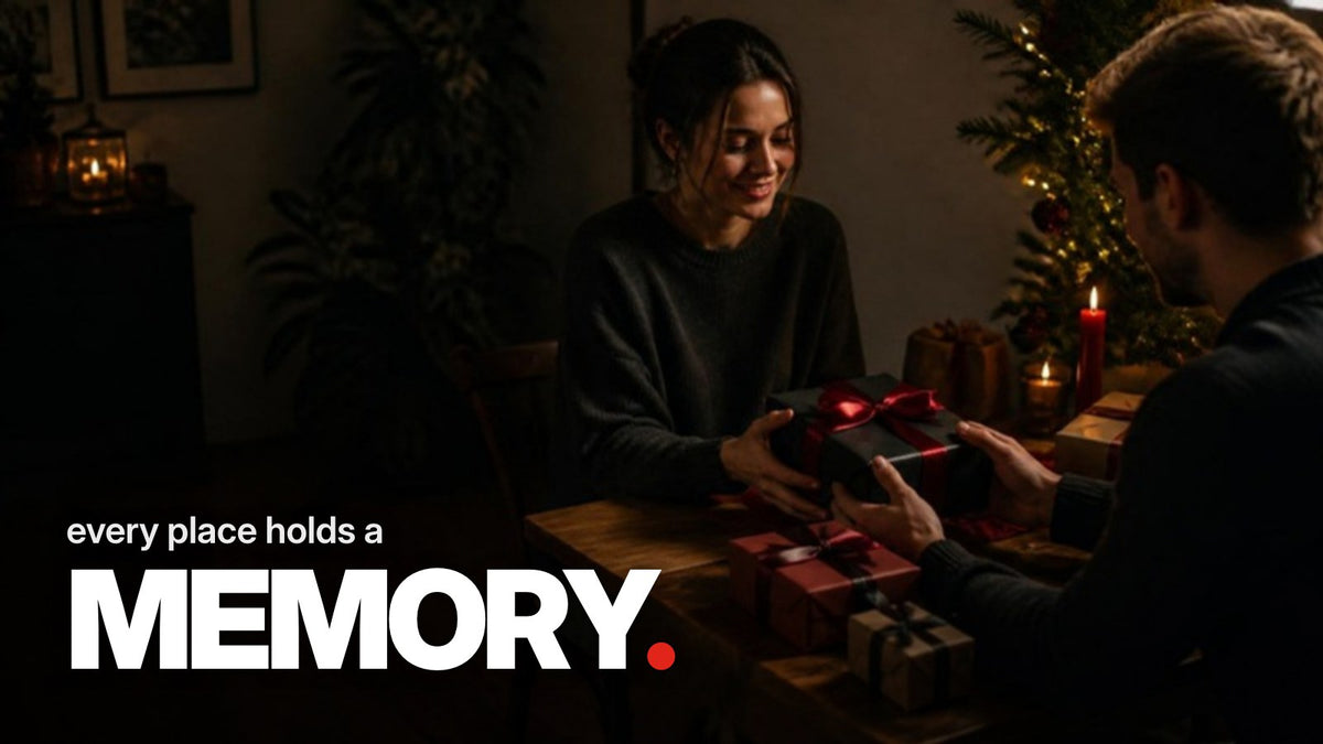Schriftzug ‚every place holds a MEMORY.‘ über einem dunklen Foto, auf dem sich bei Kerzenlicht die Hände eines Mannes und einer Frau nach einem in schwarzes Papier mit roter Schleife verpackten Wichtelgeschenk ausstrecken.