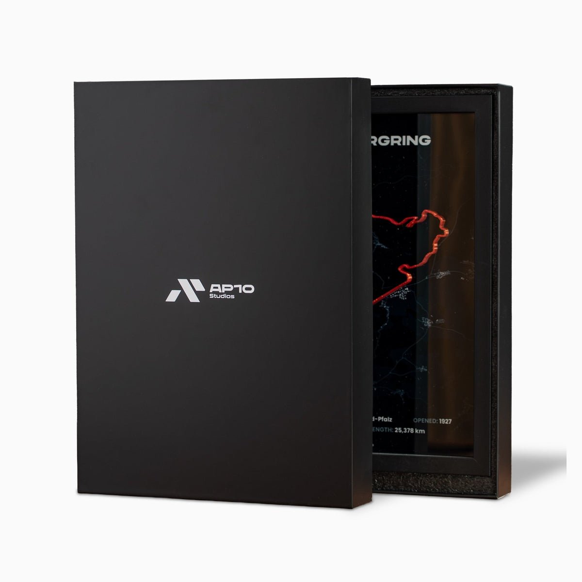 Premium-Geschenkverpackung: schwarze Box mit AP10-Studios-Logo, dahinter ein Nürburgring-Rahmen in Schaumstoffeinlage